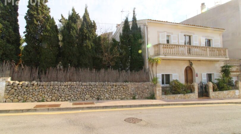 Außenansicht einer mediterranen Villa in Alcúdia mit Balkon, Natursteinmauer und Zypressen nahe Hafen.