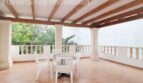 Überdachte Terrasse der Villa in Alcúdia mit Holzbalken, Säulen, weißen Gartenmöbeln und Gartenblick.