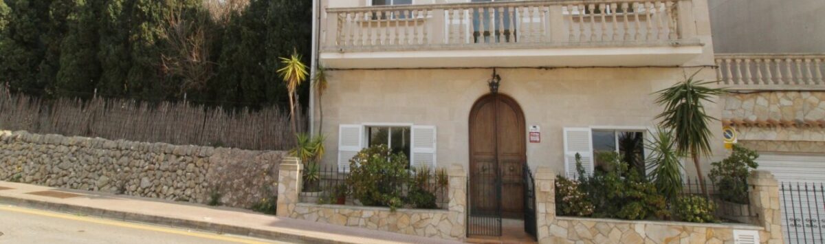 Zweigeschossige Villa in Alcúdia mit Balkon, Natursteinmauer und großem Holzeingangstor nahe dem Hafen.