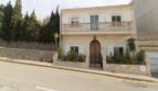 Zweigeschossige Villa in Alcúdia mit Balkon, Natursteinmauer und großem Holzeingangstor nahe dem Hafen.