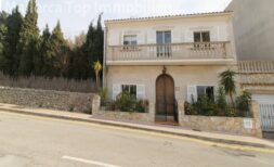 Zweigeschossige Villa in Alcúdia mit Balkon, Natursteinmauer und großem Holzeingangstor nahe dem Hafen.