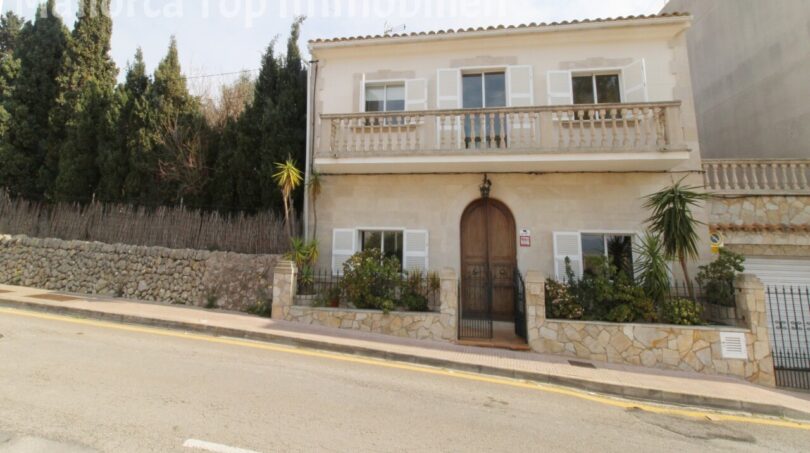 Zweigeschossige Villa in Alcúdia mit Balkon, Natursteinmauer und großem Holzeingangstor nahe dem Hafen.