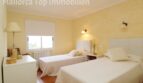 Helles Schlafzimmer der Villa in Alcúdia mit zwei Einzelbetten, gelben Wänden und Terrakottaboden.