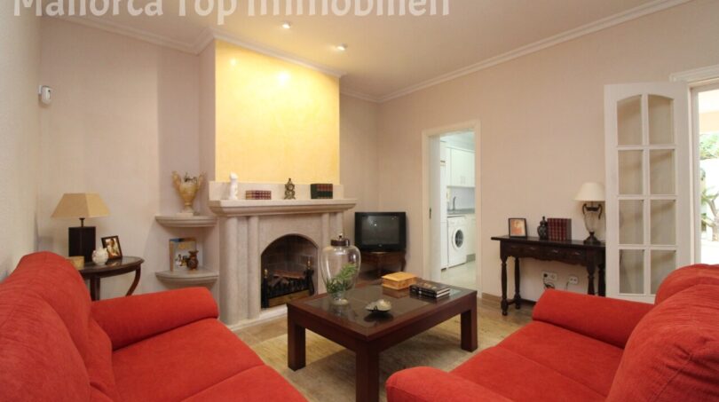 Wohnzimmer der Villa in Alcúdia mit roten Sofas, Kamin und Durchgang zur Küche