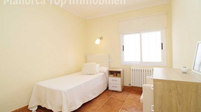 Helles Schlafzimmer der Villa in Alcúdia mit Einzelbett, Nachttisch, Heizkörper und Fenster.