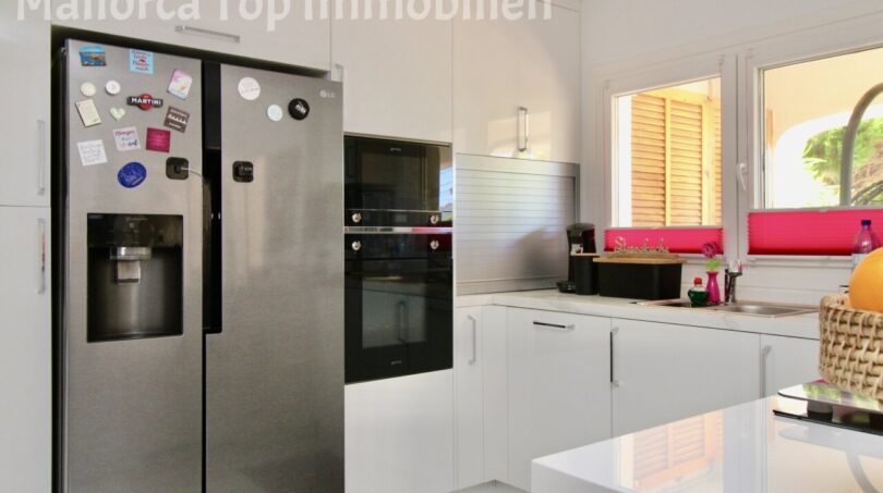 Moderne weiße Küche mit LG Side-by-Side-Kühlschrank, Einbauofen und Fenster zur Terrasse in Doppelhaushälfte Llucmajor