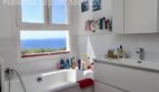 Helles weißes Badezimmer mit Badewanne und atemberaubendem Meerblick durch großes Fenster in Llucmajor