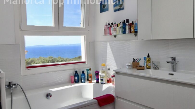 Helles weißes Badezimmer mit Badewanne und atemberaubendem Meerblick durch großes Fenster in Llucmajor