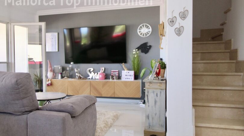 Wohnzimmer der Doppelhaushälfte in Llucmajor mit TV-Wand, Holzkommode und Treppenaufgang