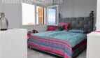 Helles Schlafzimmer mit Doppelbett, grauem Polsterkopfteil und bunter Bettwäsche, Fenster mit Meerblick