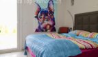 Schlafzimmer der Doppelhaushälfte in Llucmajor mit Doppelbett, bunter Bettwäsche und farbenfrohem Hunde-Kunstwerk.