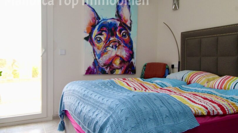 Schlafzimmer der Doppelhaushälfte in Llucmajor mit Doppelbett, bunter Bettwäsche und farbenfrohem Hunde-Kunstwerk.