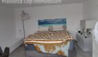 Helles Schlafzimmer mit Doppelbett, gestreifter Tagesdecke und Meerblick-Wandbild in moderner Doppelhaushälfte Llucmajor