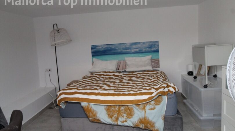 Helles Schlafzimmer mit Doppelbett, gestreifter Tagesdecke und Meerblick-Wandbild in moderner Doppelhaushälfte Llucmajor