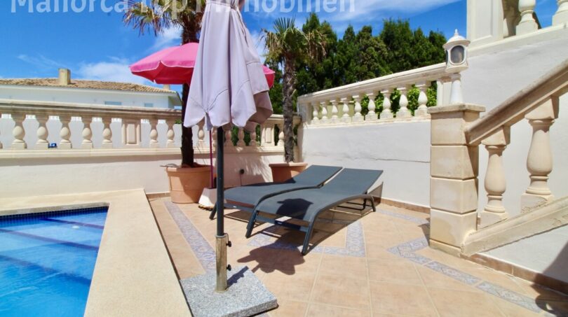 Sonnige Poolterrasse der Doppelhaushälfte in Llucmajor mit Liegestühlen, Sonnenschirm und weißer Balustrade