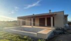 Neubau-Finca in Manacor mit überdachter Terrasse und leerem Pool, klarer Himmel, ländliche Umgebung.