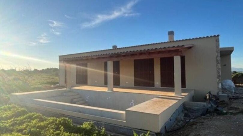 Neubau-Finca in Manacor mit überdachter Terrasse und leerem Pool, klarer Himmel, ländliche Umgebung.
