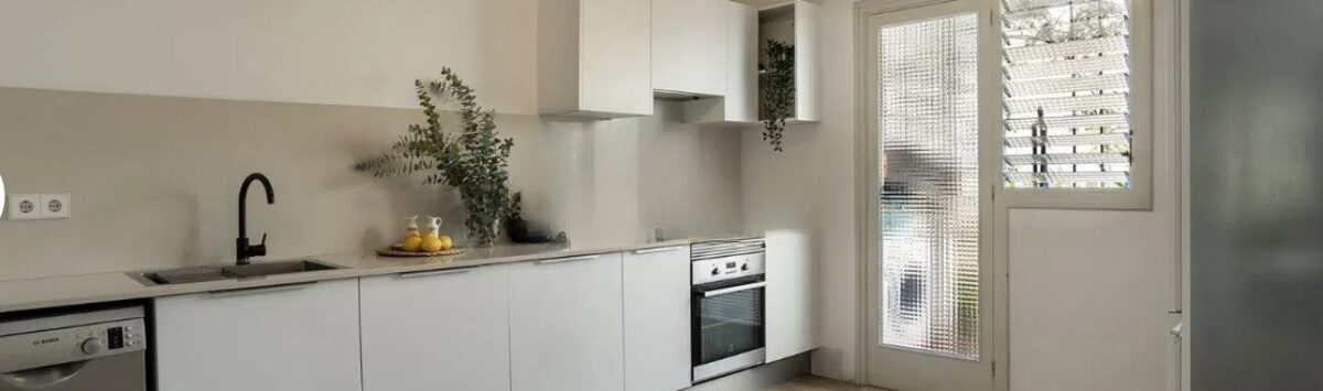 Helle Küche mit weißen Fronten, Einbaugeräten und Holzboden in moderner Wohnung in Palma de Mallorca