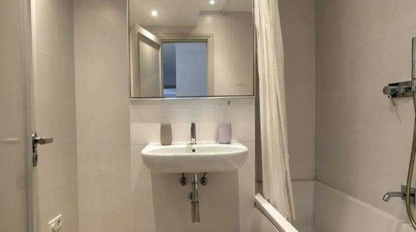 Helles Badezimmer der modernen Wohnung in Palma mit Badewanne, Wandwaschbecken und Spiegel.