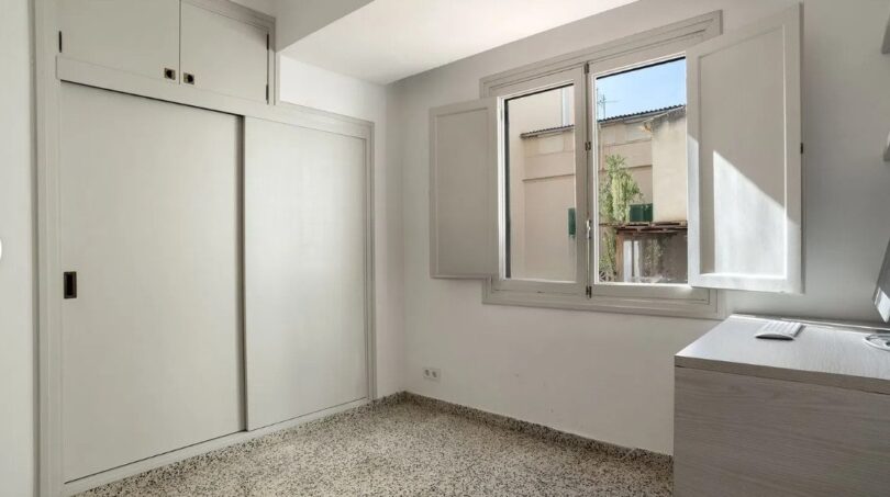 Helles Schlafzimmer mit Einbauschrank, Terrazzoboden und Fenster mit Blick auf Innenhof in Palma