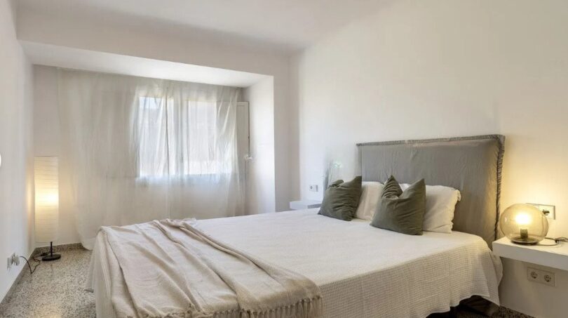 Helles Schlafzimmer mit Doppelbett, grauem Polsterkopfteil und weißen Wänden in moderner Wohnung in Palma de Mallorca.