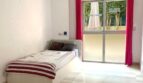 Helles Schlafzimmer mit Einzelbett, roten Vorhängen und Terrassenzugang in Erdgeschosswohnung Palma