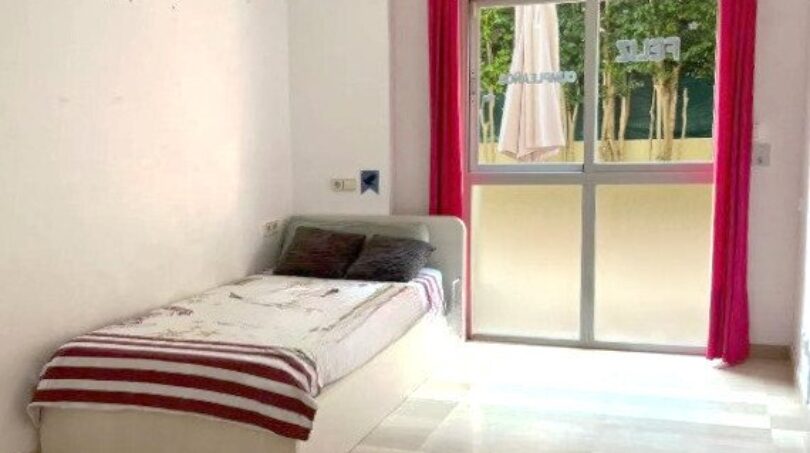 Helles Schlafzimmer mit Einzelbett, roten Vorhängen und Terrassenzugang in Erdgeschosswohnung Palma