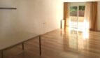 Helles, leeres Wohnzimmer mit Holzparkett, großem Fenster und goldenen Vorhängen in Erdgeschosswohnung Palma