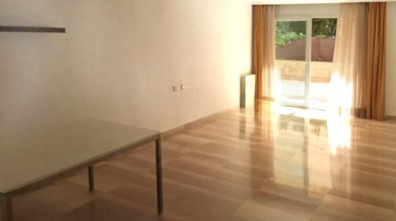 Helles, leeres Wohnzimmer mit Holzparkett, großem Fenster und goldenen Vorhängen in Erdgeschosswohnung Palma