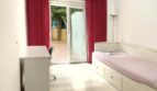 Helles Schlafzimmer mit Einzelbett, Schreibtisch und Terrassenzugang mit roten Vorhängen in Erdgeschosswohnung Palma