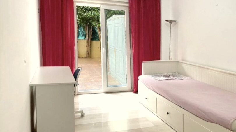 Helles Schlafzimmer mit Einzelbett, Schreibtisch und Terrassenzugang mit roten Vorhängen in Erdgeschosswohnung Palma