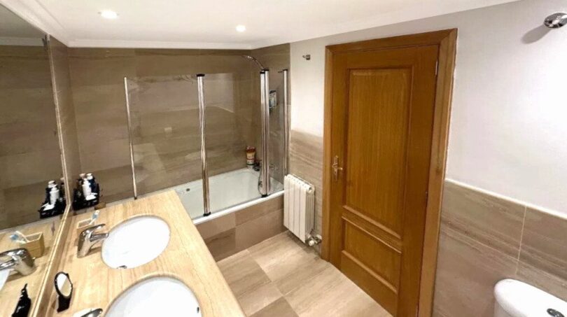Helles Badezimmer mit Doppelwaschbecken, Badewanne mit Dusche, Holztür und Heizkörper in Erdgeschosswohnung Palma