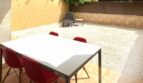 Sonnige Terrasse mit weißem Tisch, roten Stühlen und Kiesgarten, umgeben von begrünten Mauern in Palma
