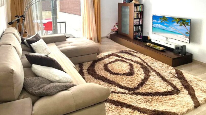 Helles Wohnzimmer mit großem Ecksofa, Flachtisch-TV und gemustertem Teppich in Erdgeschosswohnung Palma