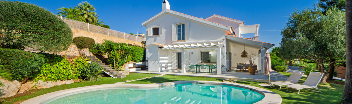 Villa Nova Santa Ponça: Casa blanca con piscina ovalada, terraza con pérgola y jardín cuidado en ubicación exclusiva.