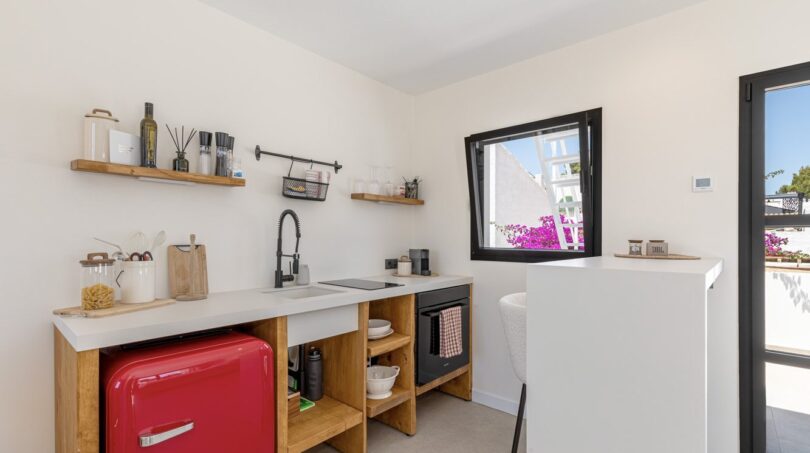 Moderne Küche der Mallorca-Villa mit rotem Retro-Kühlschrank, Holzregalen und Fenster mit Bougainvillea-Blick