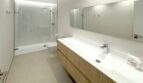 Modernes Badezimmer mit großer Glasdusche, Holzunterschrank, weißem Doppelwaschbecken und Spiegel in Erstbezugswohnung Palma