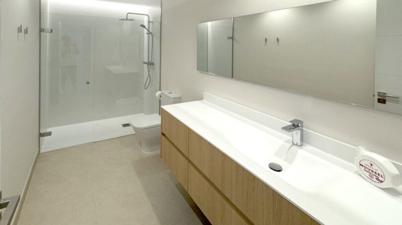 Modernes Badezimmer mit großer Glasdusche, Holzunterschrank, weißem Doppelwaschbecken und Spiegel in Erstbezugswohnung Palma