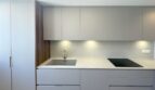 Moderne Einbauküche mit grau-matten Fronten, weißer Steinarbeitsplatte, Induktionskochfeld und Unterbodenbeleuchtung