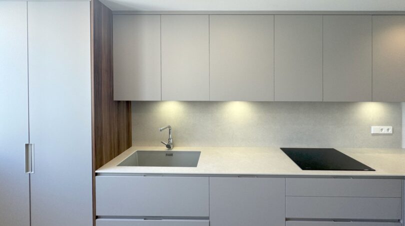 Moderne Einbauküche mit grau-matten Fronten, weißer Steinarbeitsplatte, Induktionskochfeld und Unterbodenbeleuchtung