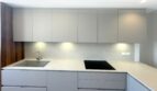 Moderne Einbauküche mit hellgrauen Fronten, Kochfeld, Spüle und Unterbauleuchten in Erstbezug-Wohnung Palma