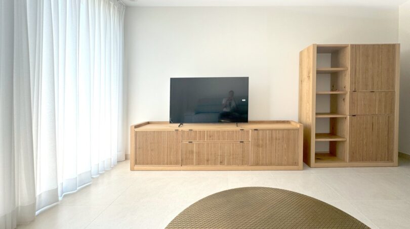 Helles Wohnzimmer mit Eichenholz-TV-Möbel, Regalschrank und bodenlangen Vorhängen in Erstbezugswohnung Palma