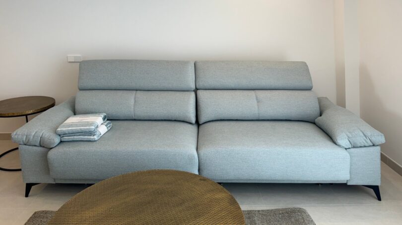 Helles Wohnzimmer mit hellblauem Designsofa und goldenem Couchtisch in exklusiver Neubauwhg Palma