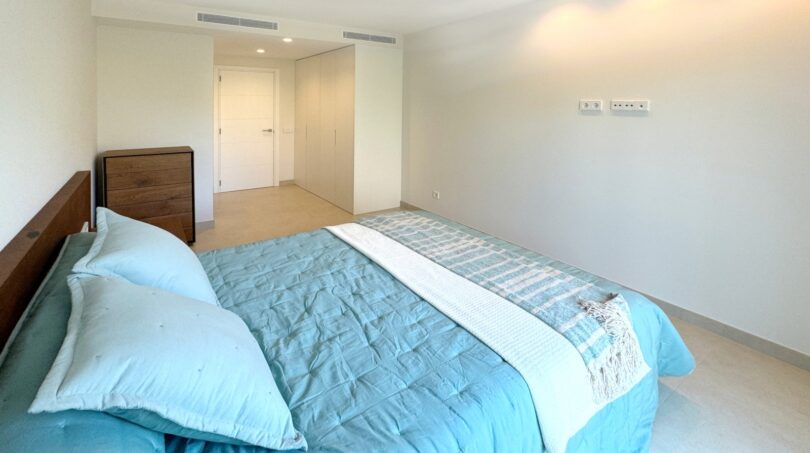 Helles Schlafzimmer mit türkisem Doppelbett, Holzkommode und modernem Einbauschrank in Palma-Neubau