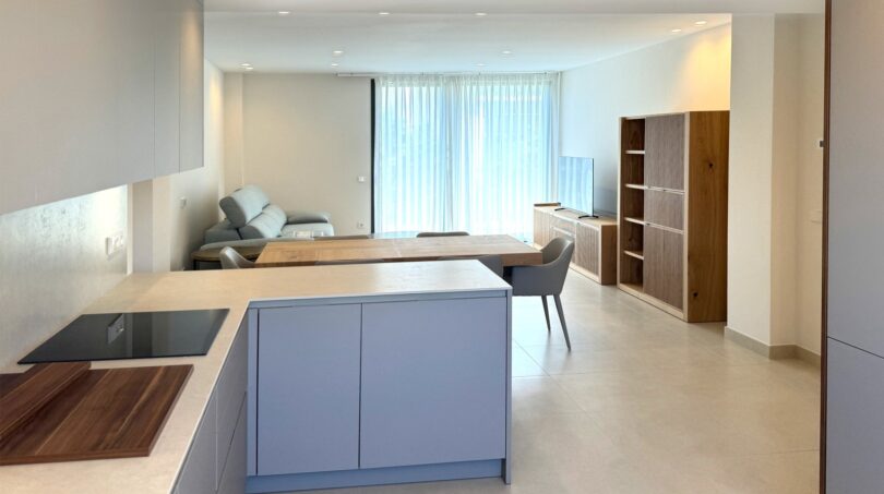Moderner offener Wohn-Kochbereich mit grauer Kücheninsel, Esstisch und Holzregal in Erstbezugswohnung Palma