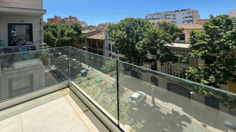 Moderner Glasbalkon mit Blick auf baumgesäumte Straße und Altstadt-Architektur in Palma de Mallorca