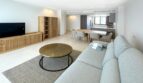 Helles Wohnzimmer mit grauem Sofa, rundem Couchtisch und offener Küche in exklusiver Erstbezugswohnung in Palma