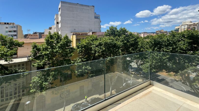 Moderne Dachterrasse mit Glasgeländer und Blick auf baumgesäumte Straße in Palma de Mallorca