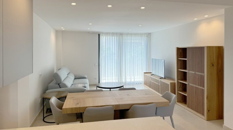 Heller Wohn-Essbereich mit Holztisch, grauem Sofa, TV-Möbel und Raumteiler in exklusiver Erstbezug-Wohnung Palma