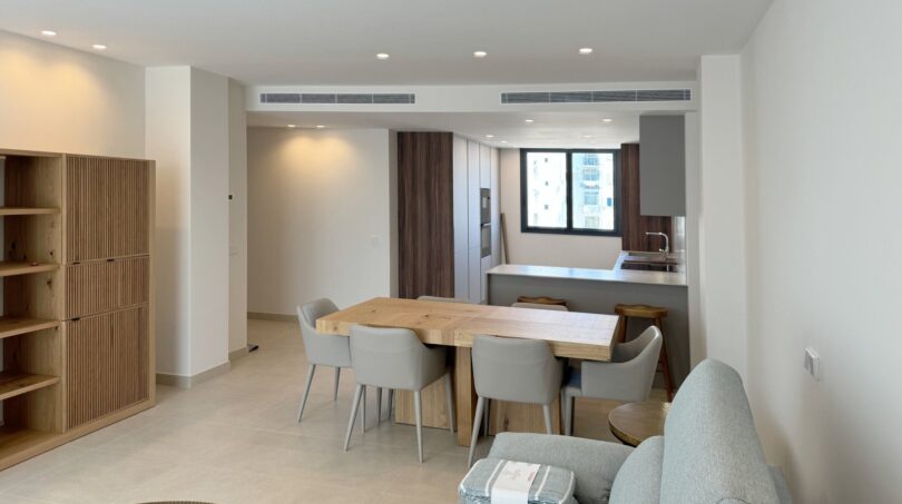 Moderner Wohn-Essbereich mit Holztisch, grauer Küche und elegantem Sideboard in exklusiver Neubauwohnung Palma